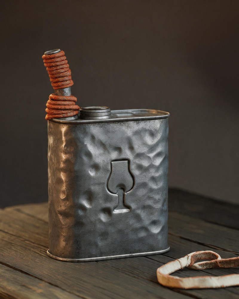 A small dented tin oil can with a twisted wire bail, standing on rough planks beside a coil of leather cord.